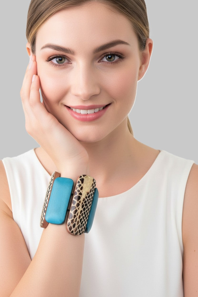 A close-up view of a model wearing a wide wood stretch bracelet featuring varying length turquoise panels and a central animal print patterned link.