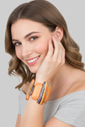 A close-up view of a smiling model wearing an artistic wood stretch bracelet featuring varying length orange and abstract striped panels.