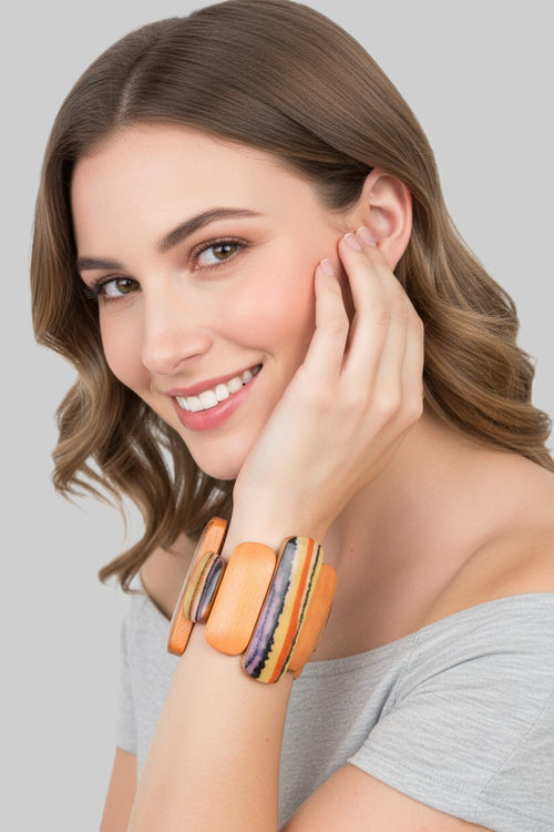 A close-up view of a smiling model wearing an artistic wood stretch bracelet featuring varying length orange and abstract striped panels.