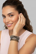 A close-up view of a model wearing a glamorous multi-strand bracelet featuring bronze crystal pearls, gunmetal chains, and woven gray 