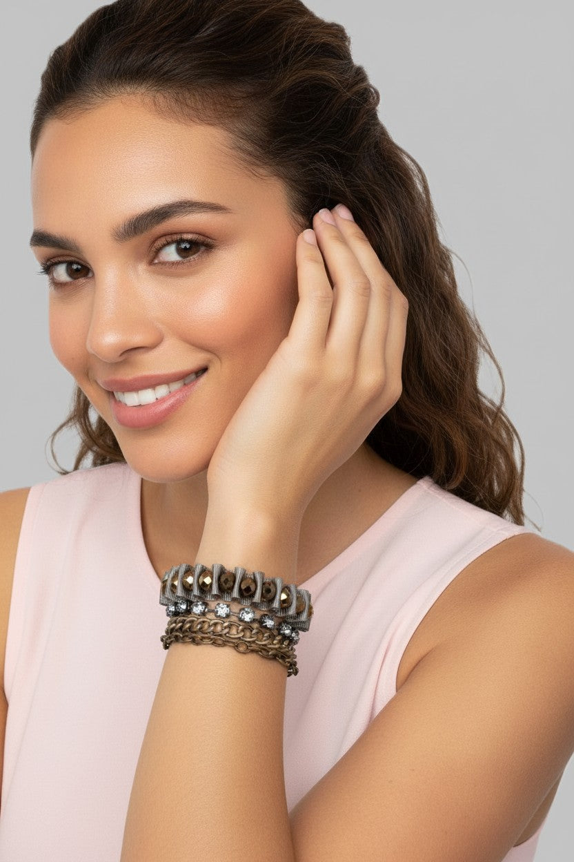 A close-up view of a model wearing a glamorous multi-strand bracelet featuring bronze crystal pearls, gunmetal chains, and woven gray 