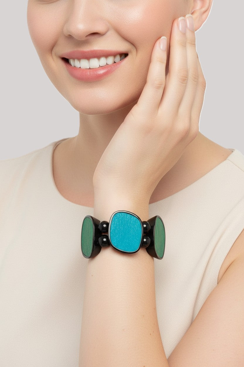 A close-up view of a model wearing a multi strand black bead stretch bracelet featuring vibrant turquoise blue and forest green shell inlay panels.