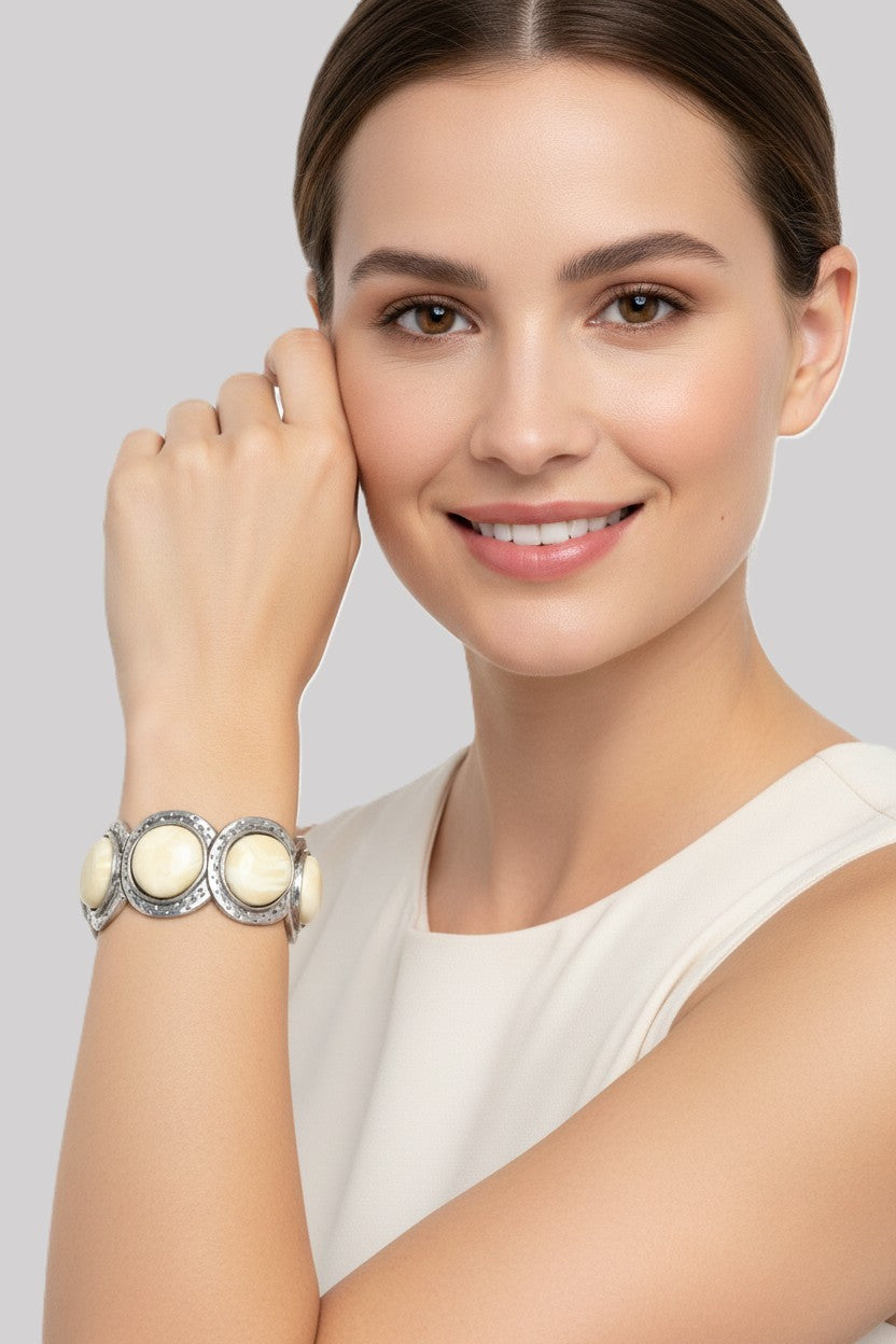 A close-up view of a smiling model wearing a textured silver plated stretch link bracelet set with large smooth cream cabochon stones.