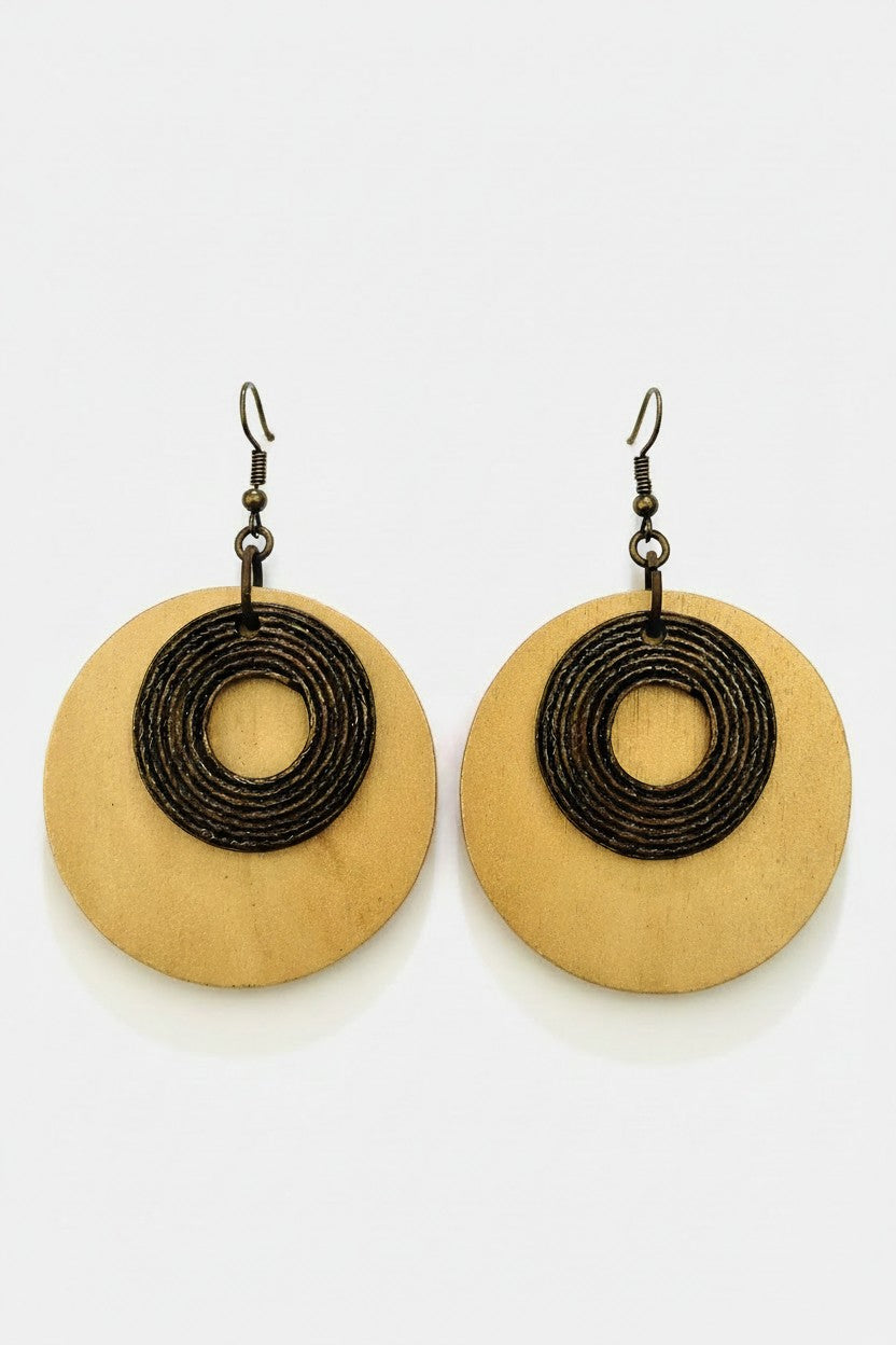 A pair of dangle earrings featuring round, light tan wood discs with a metal coiled spiral design in the center, suspended from dark metal fishhook wires, set against a plain white background.