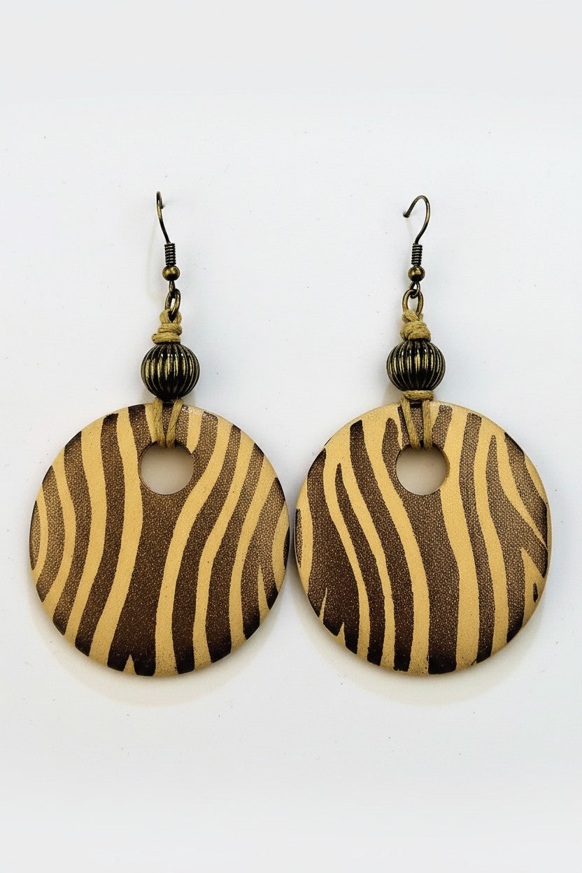 A pair of bohemian-style dangle earrings featuring round wooden disc charms with a brown and beige zebra stripe pattern, suspended from dark metal hooks with small beads.