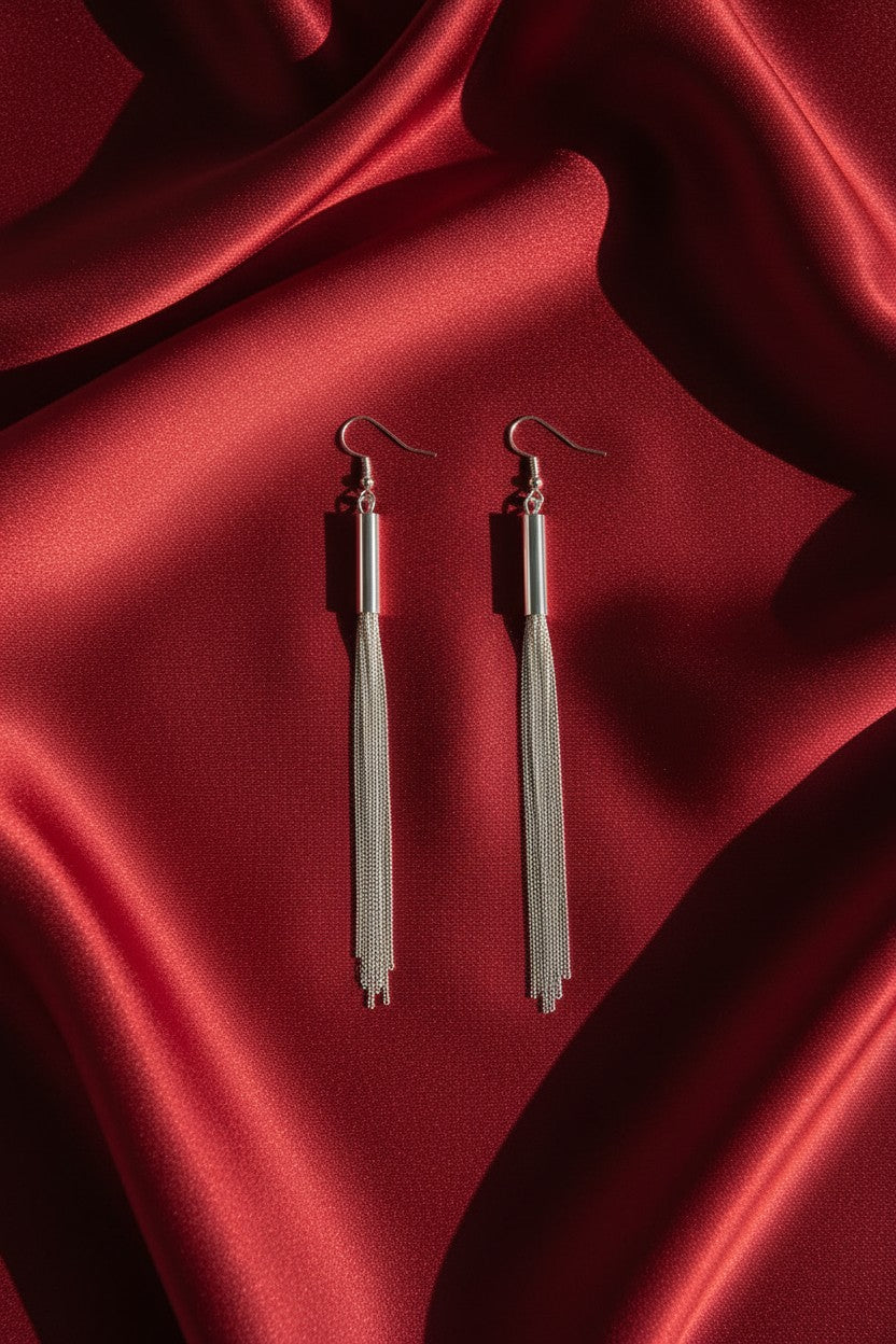 A pair of silver-toned tassel drop earrings with fishhook backs, displayed on draped red satin fabric.