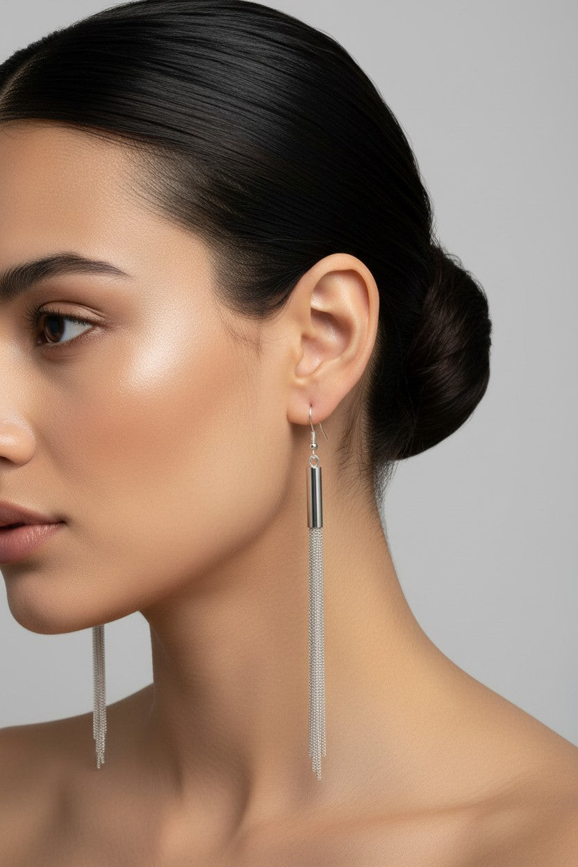 Woman wearing elegant silver plated drop earrings featuring a sleek polished tube and fine liquid chain tassels.