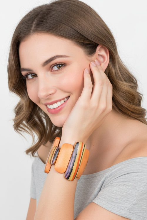 A close-up view of a smiling model wearing an artistic wood stretch bracelet featuring varying length orange and abstract striped panels.