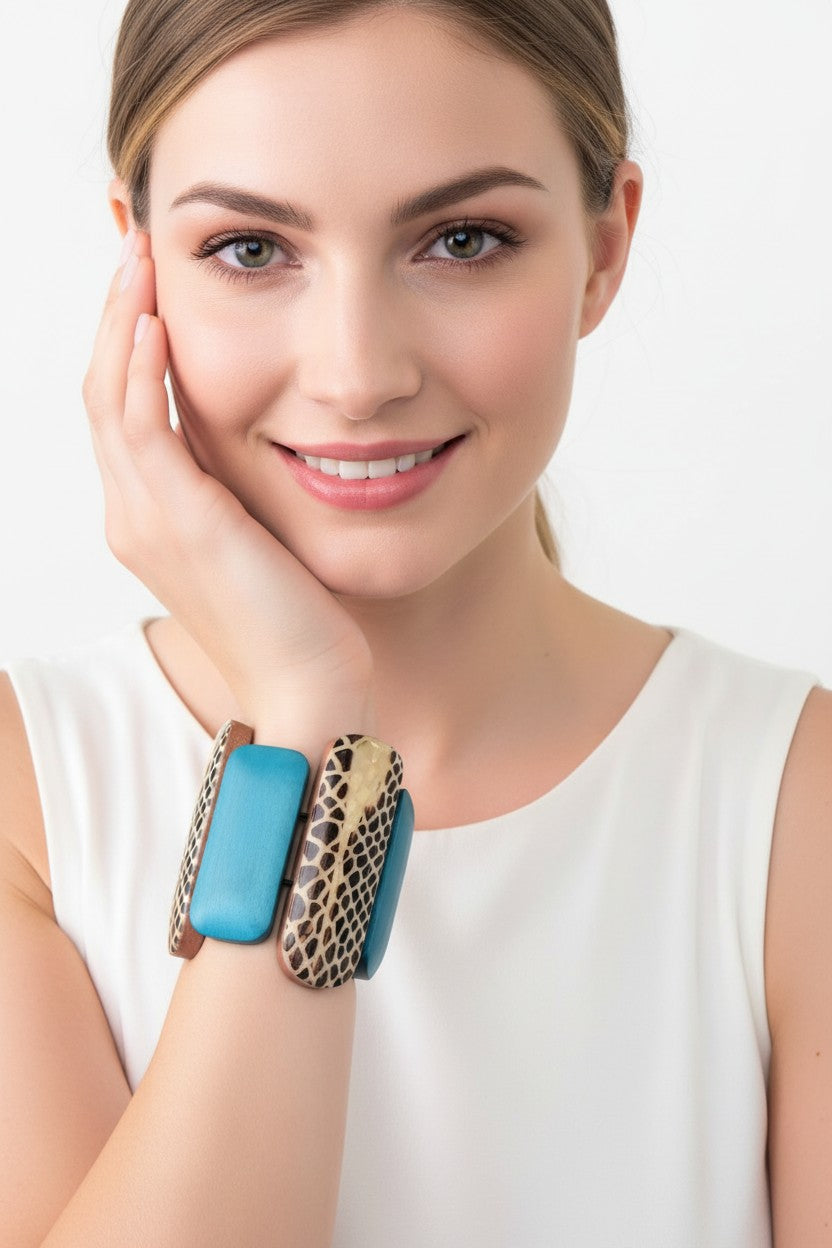 A close-up view of a model wearing a wide wood stretch bracelet featuring varying length turquoise panels and a central animal print patterned link.