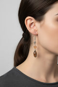 Side profile view of a model wearing a unique Australian Made silver plated drop earring adorned with a faceted amber Swarovski crystal and a smoky brown oval bead.