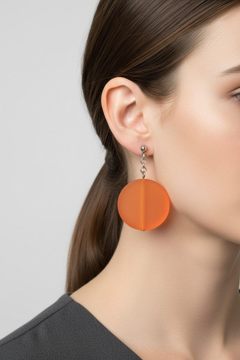 Close up side profile of a model wearing a pair of Australian Made silver plated chain drop earrings featuring large frosted orange circular disc beads.