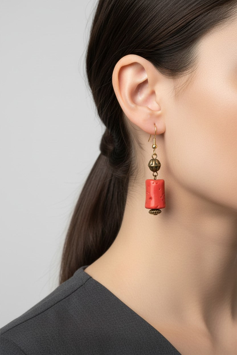 Side profile view of a model wearing a pair of Australian Made gold drop earrings featuring a textured, cylindrical matte red coral style focal bead.