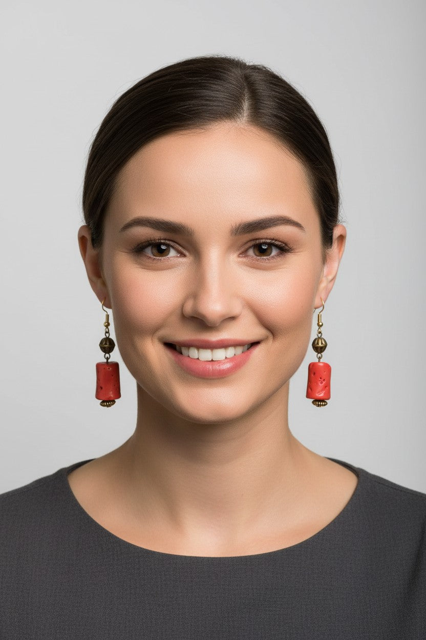 front profile view of a model wearing a pair of Australian Made gold drop earrings featuring a textured, cylindrical matte red coral style focal bead.