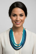 Long multi-strand beaded necklace with varying blue tones on multiple blue cords against a light grey background.