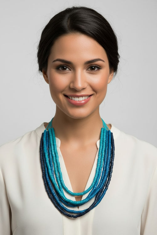 Long multi-strand beaded necklace with varying blue tones on multiple blue cords against a light grey background.