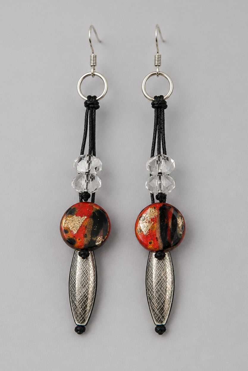 Long bohemian drop earrings for pierced ears featuring black cords, faceted clear crystal-look beads, red and black abstract discs with silver foil, and textured silver oval beads.