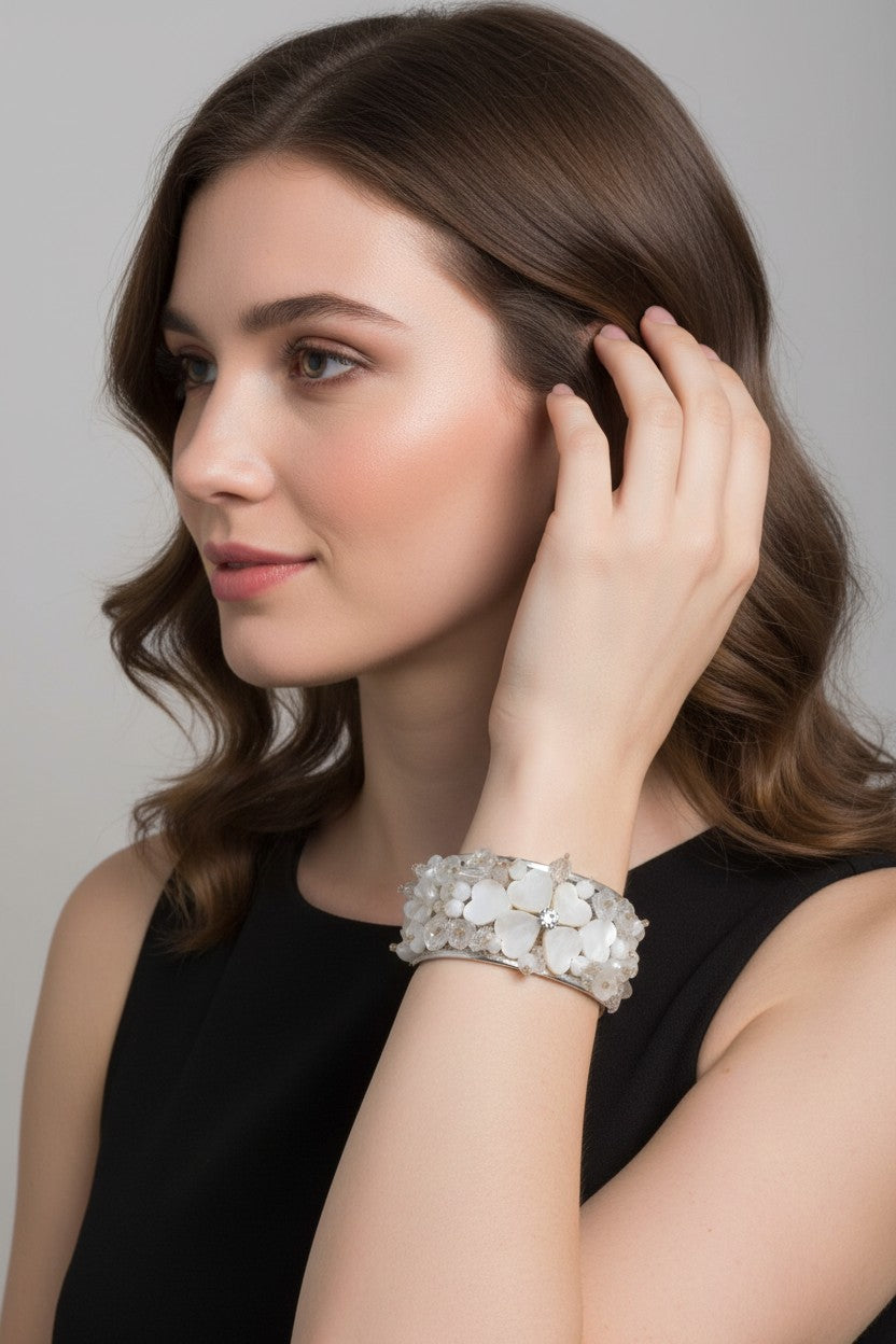 A model wearing an elegant white variant of the shell wide cuff bracelet featuring iridescent mother-of-pearl shell pieces and clear glass beads against a black dress.