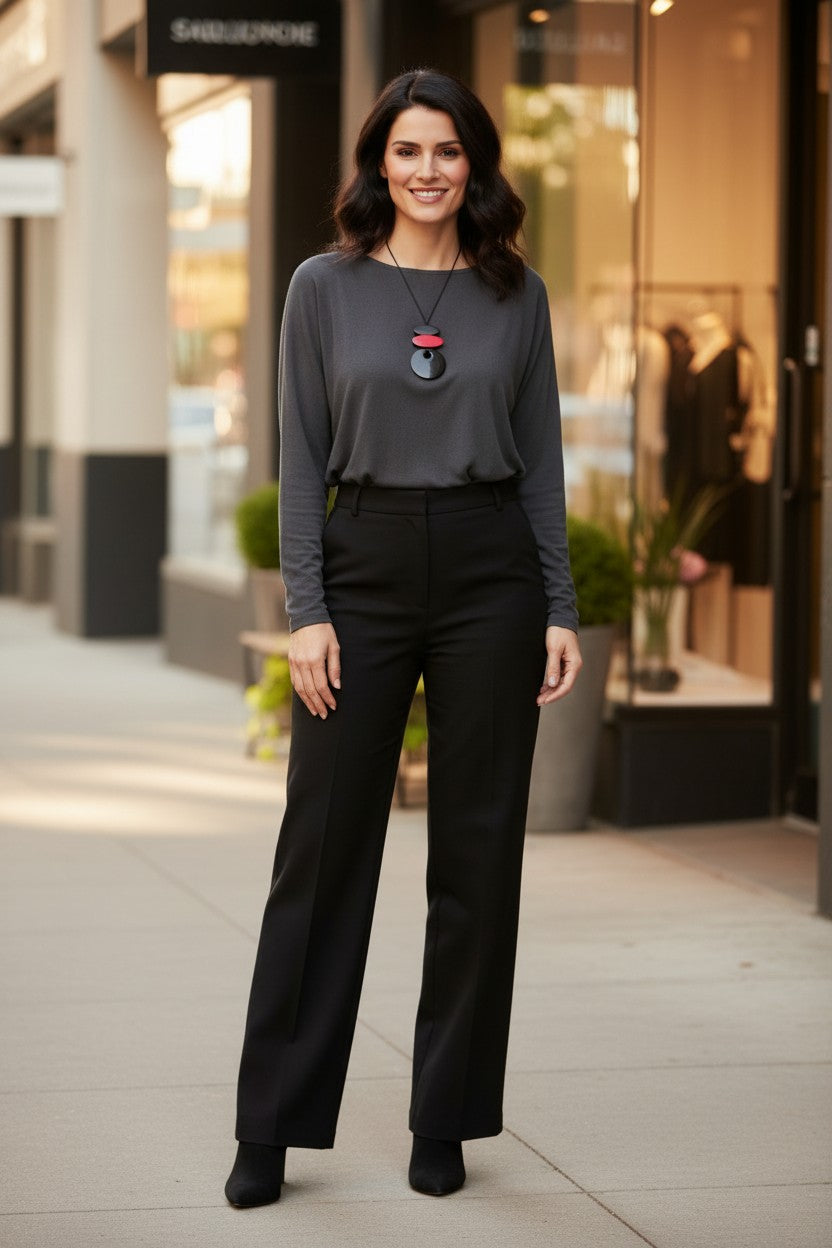 Woman standing in front of shops wearing a geometric statement necklace featuring a vibrant fuchsia pink oval piece and black components connected to a glossy black pendant on an adjustable cord.