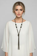 Model wearing a long gunmetal multi-chain necklace featuring a knotted tassel design, textured wire loop accents, and large silver beads with sparkling stone inlays over a white silk top.