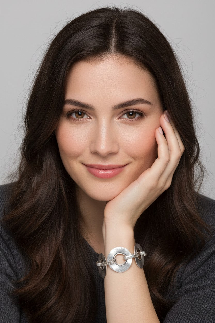  A close-up view of a model resting her chin on her hand, showcasing a silver-plated geometric disc link bracelet on her wrist.
