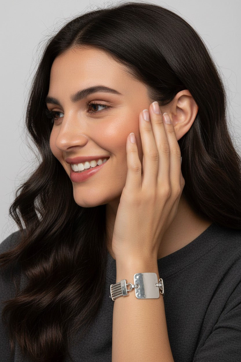 A close-up view of a smiling model showcasing a contemporary silver plated bracelet featuring a bold square metallic plate and multi strand wire links.