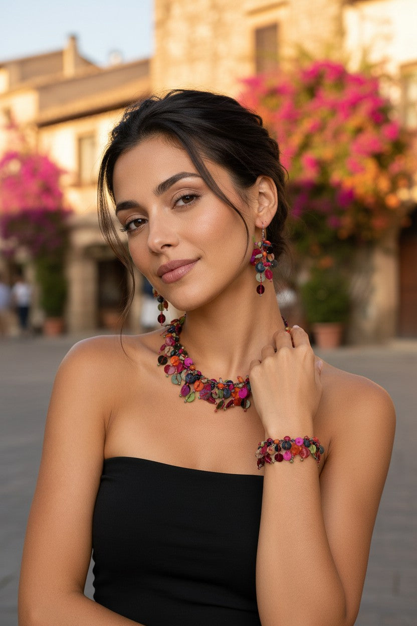Model wearing a matching multi-coloured statement jewellery set including a cluster collar necklace, a charm bracelet, and cascading drop earrings street background