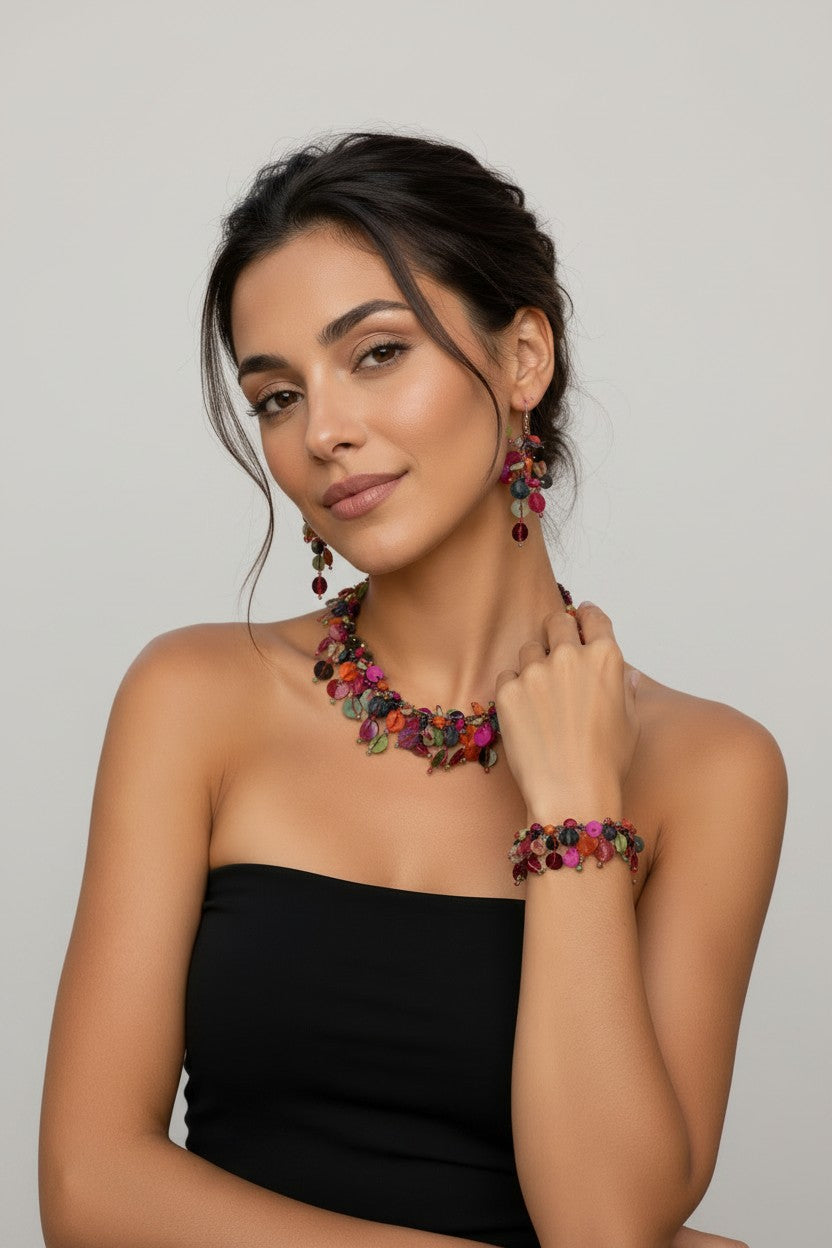 Model wearing a matching multi-coloured statement jewellery set including a cluster collar necklace, a thick charm bracelet, and cascading drop earrings featuring purple, pink, green, and orange discs.