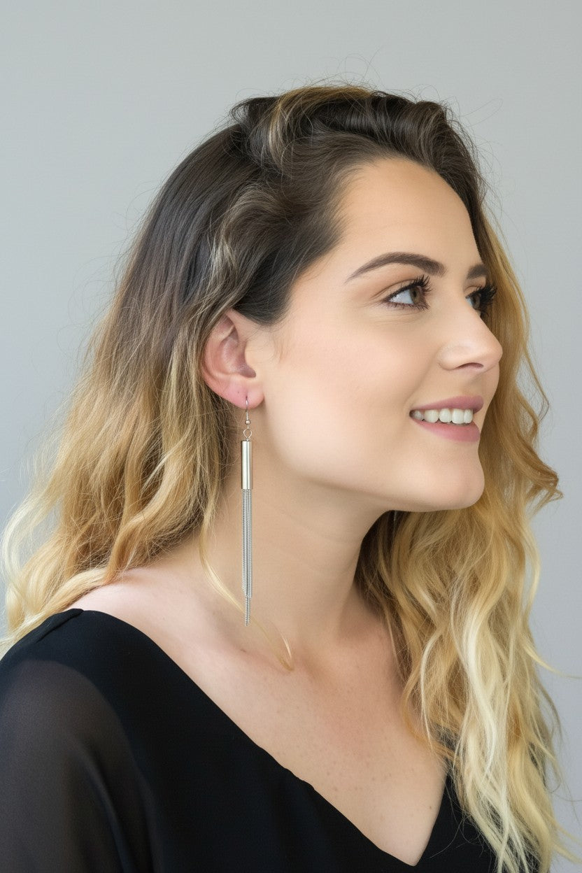 Woman wearing elegant silver plated drop earrings featuring a sleek polished tube and fine liquid chain tassels.