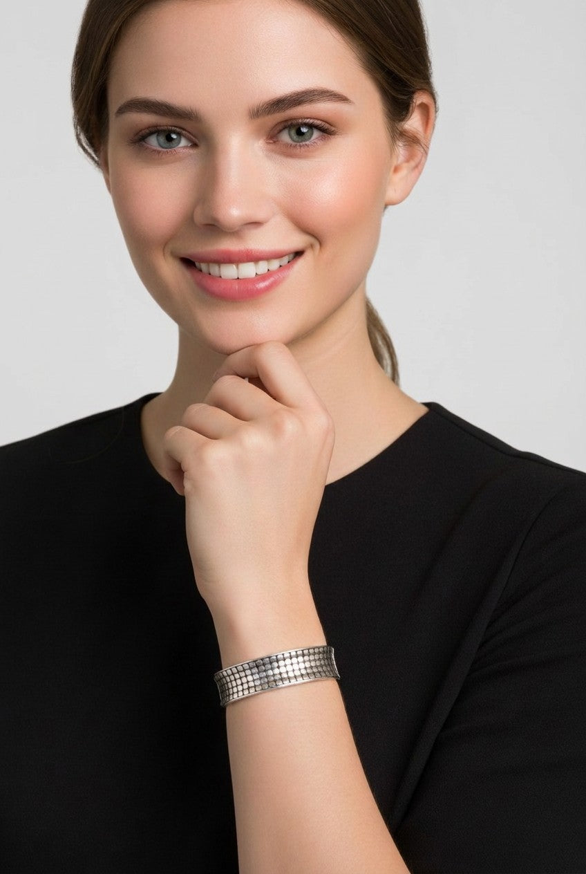 A close-up view of a smiling model showcasing a wide silver plated stretch bracelet featuring a textured grid lattice pattern on her wrist.