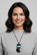 Woman wearing a geometric statement necklace featuring a vibrant turquoise blue oval piece and black components connected to a glossy black pendant on an adjustable cord.